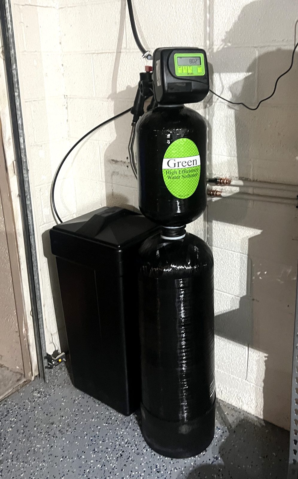 Green high-efficiency water softener installed in a home garage